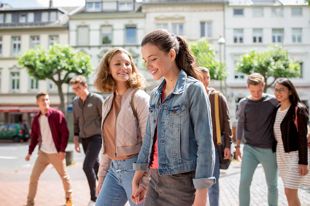 Zwei junge Frauen laufen Hand in Hand über einen Schulhof.